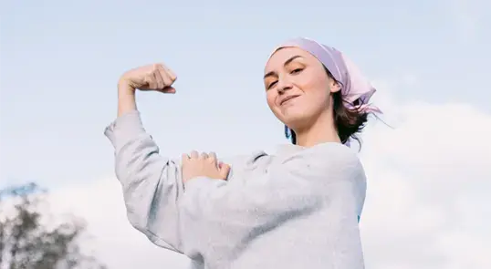 An acute lymphoblastic leukemia patient wearing a bandana over her hair flexes her bicep.